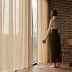vrouw kijken door gordijnen naar buiten Bregje-Nix-Concept-Styling-Interiorstyling